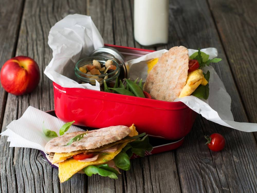 Omelett i polarbrød med grønnsaker og en liten tomat på siden, ser ut til å være en matpakke på et trebord.