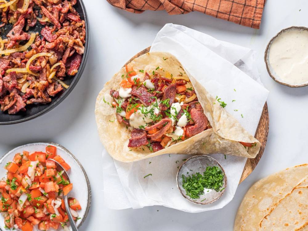 En wrap fylt med kjøtt, grønnsaker og saus, plassert på et papir med en liten skål med grønnsaker ved siden av.