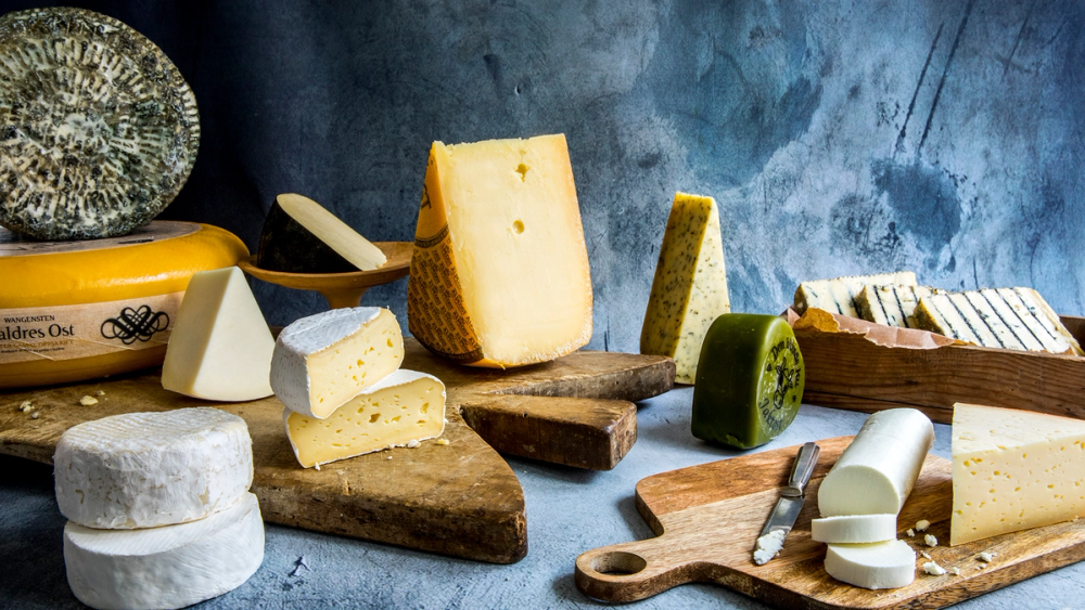 Ulike typer ost og ostekniver på et bord med en blå bakgrunn.