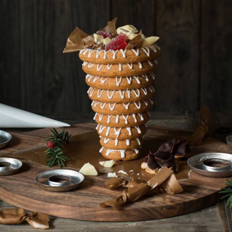 En stab med flere store kransekaker dekorert med jordbær og sjokolade, plassert på et rundt trebrett med julepynt rundt.