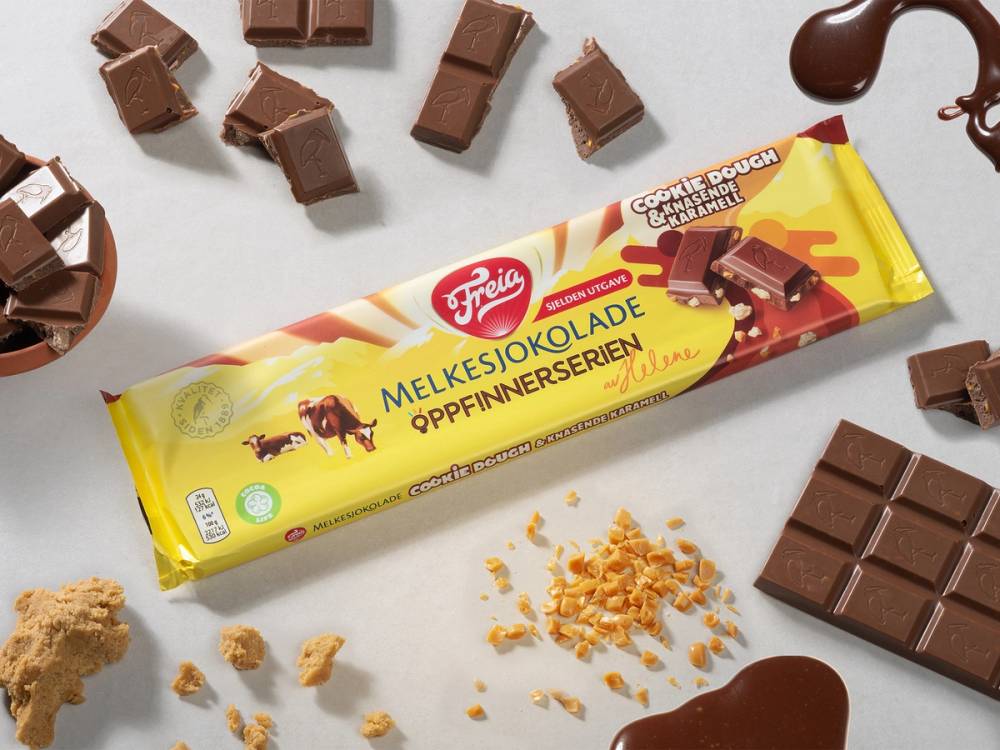 Melkesjokoladekjeks med cookie dough-smak og noen bruttestykker av sjokolade rundt på et hvitt underlag.
