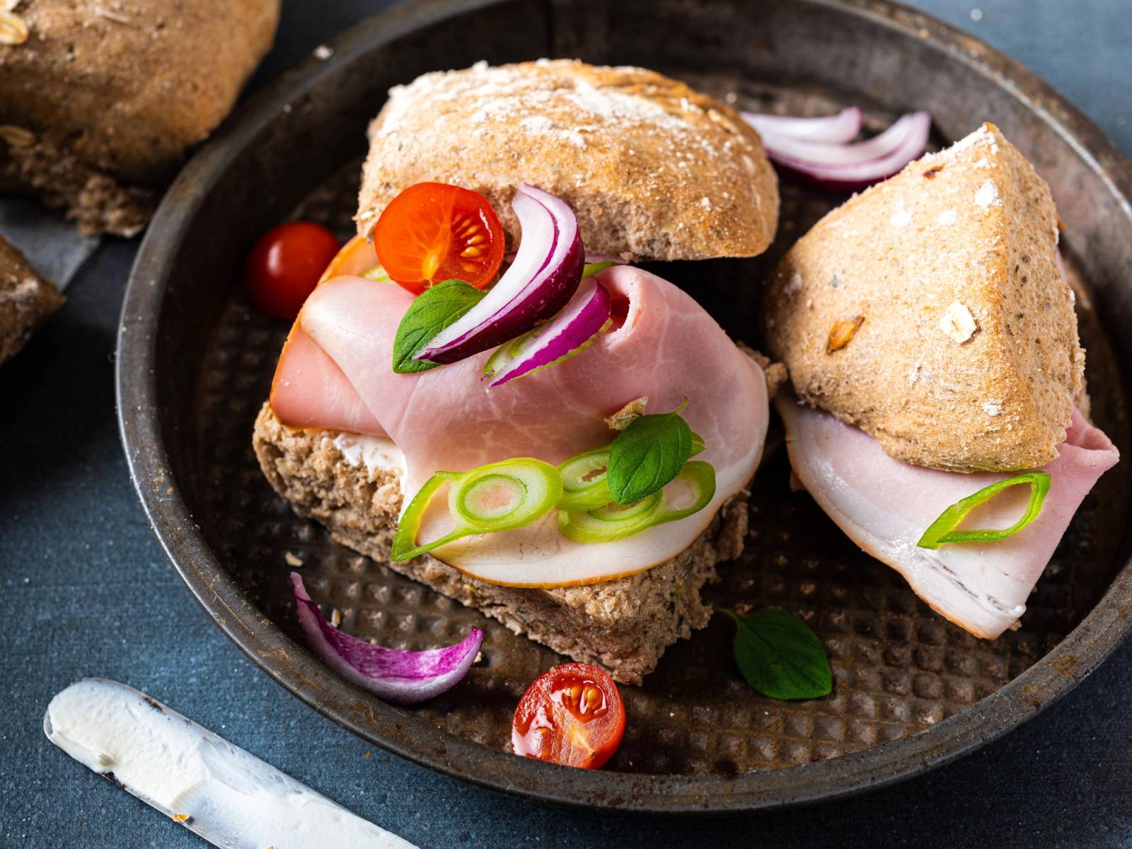 En matpakke med brød, skinke, egg, cherrytomater og løk på en tallerken