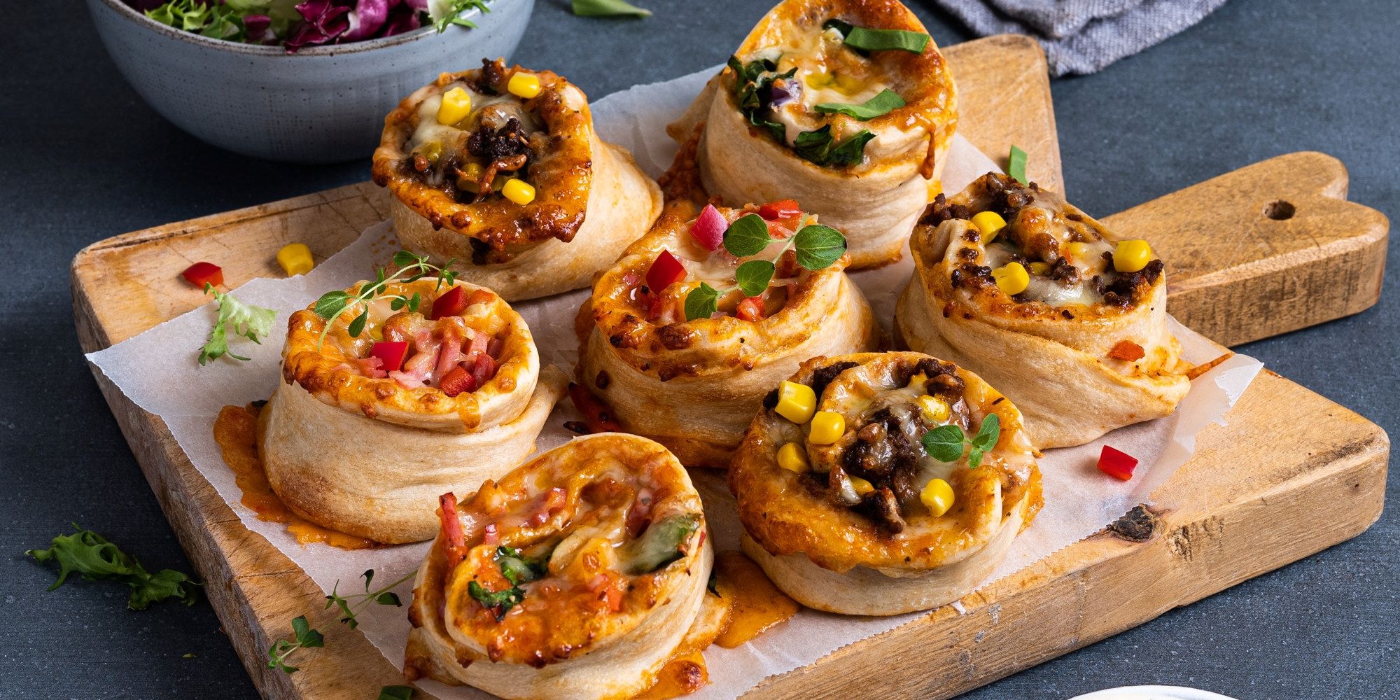 Små pizza snurrer med ulike fyll på et skjærebrett, klare til servering.