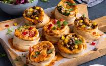 Små pizza snurrer med ulike fyll på et skjærebrett, klare til servering.