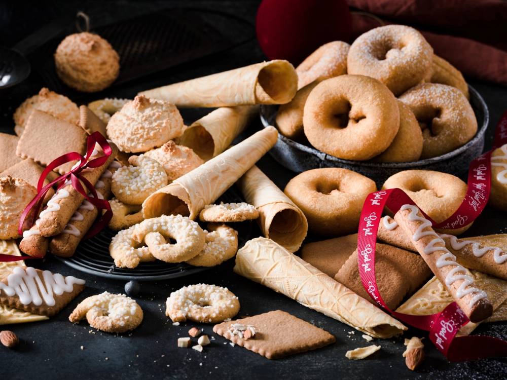 Julekaker og småkaker på et svart fat med noen kjeks og dekorative elementer rundt.