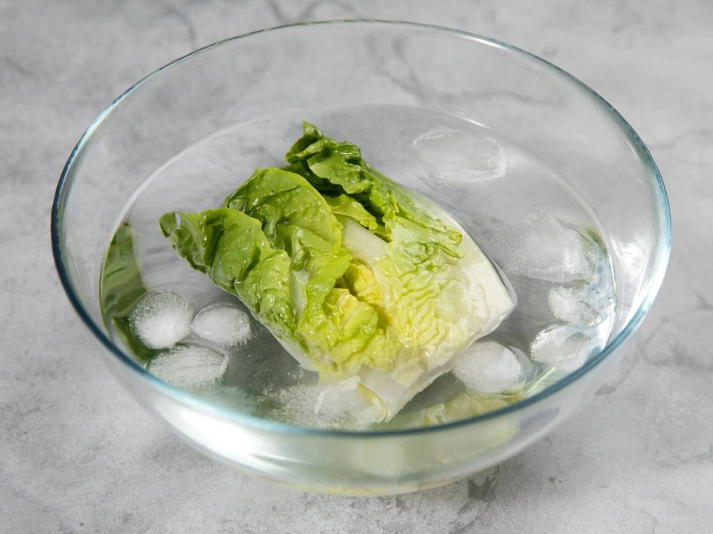 Salatblad som ligger i vann med isbiter i en glassbolle