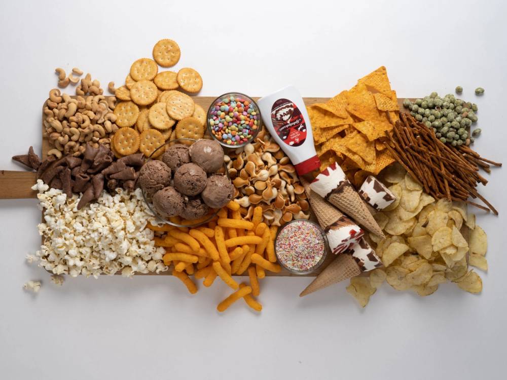 Et utvalg av ulike snacks og godteri, inkludert kjeks, sjokolade, popcorn, og smågodt, spredt ut på et hvitt underlag.