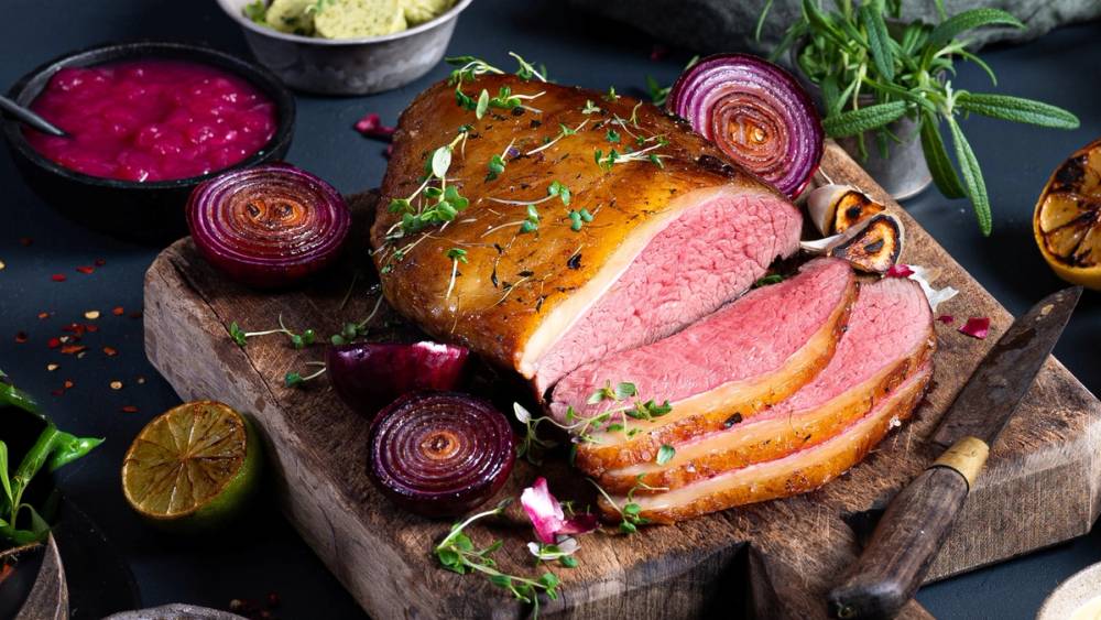 Stekt biff med rosa innside på et skjærebrett, omgitt av rødløk og urter, klar til å serveres etter en lang arbeidsuke.