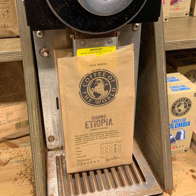 Kaffekvern som maler kaffebønner i en butikk, med en pose med etikett for Etiopia på utsiden.