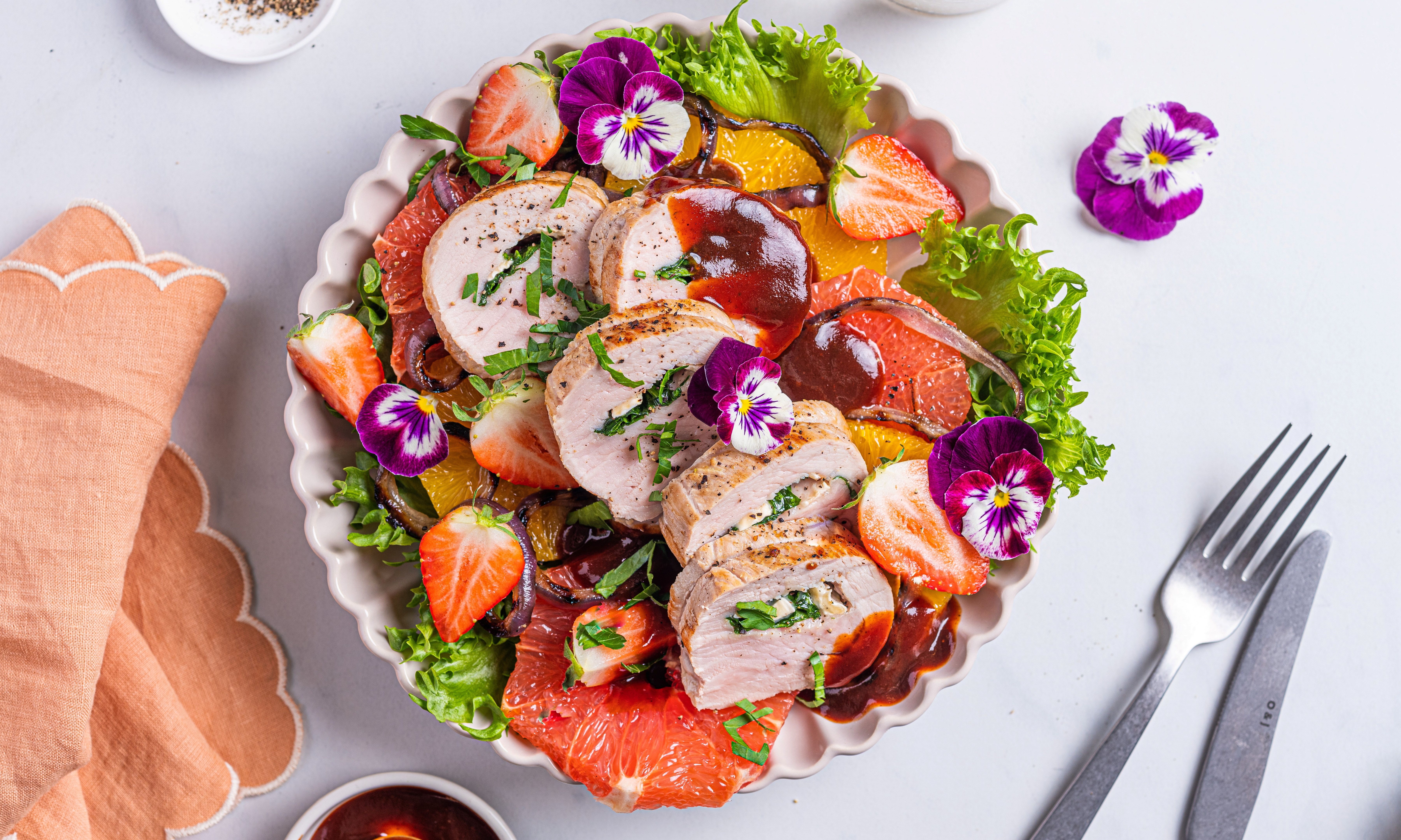 Svinefilet fylt med ost og spinat, servert på en tallerken med grønnsaker og blomsterdekorasjoner.