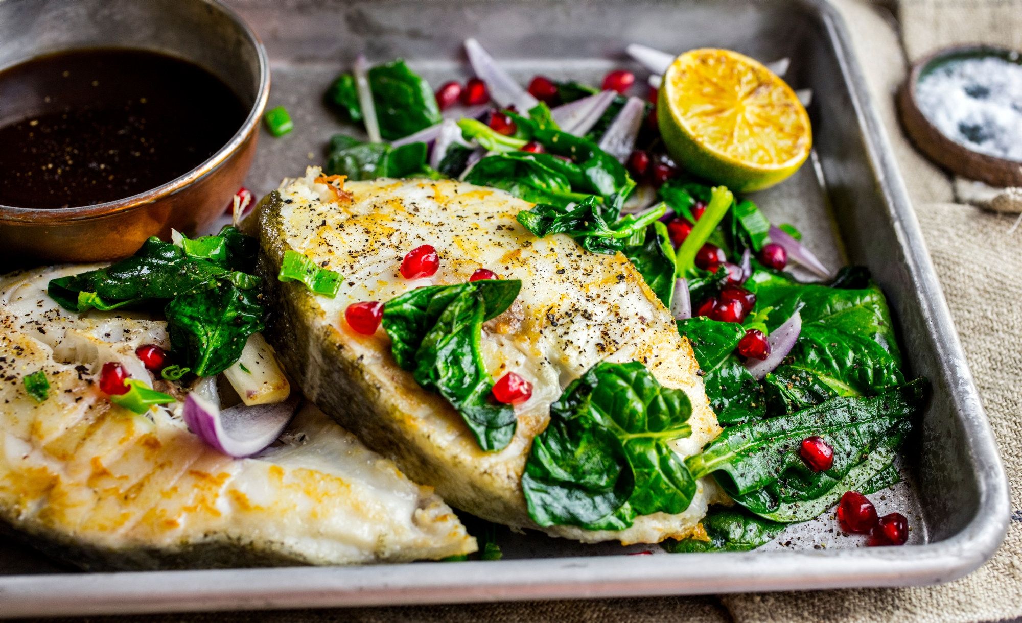 Stekt skrei med grønnsaker, sitron og granateple på et fat.