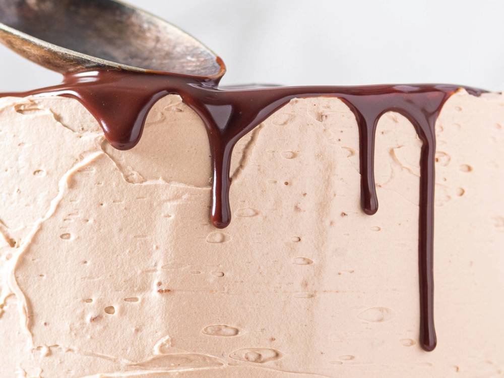 Sjokoladesaus helles over en lys iskremkake med et jevnt lag av iskrem og en glatt overflate.