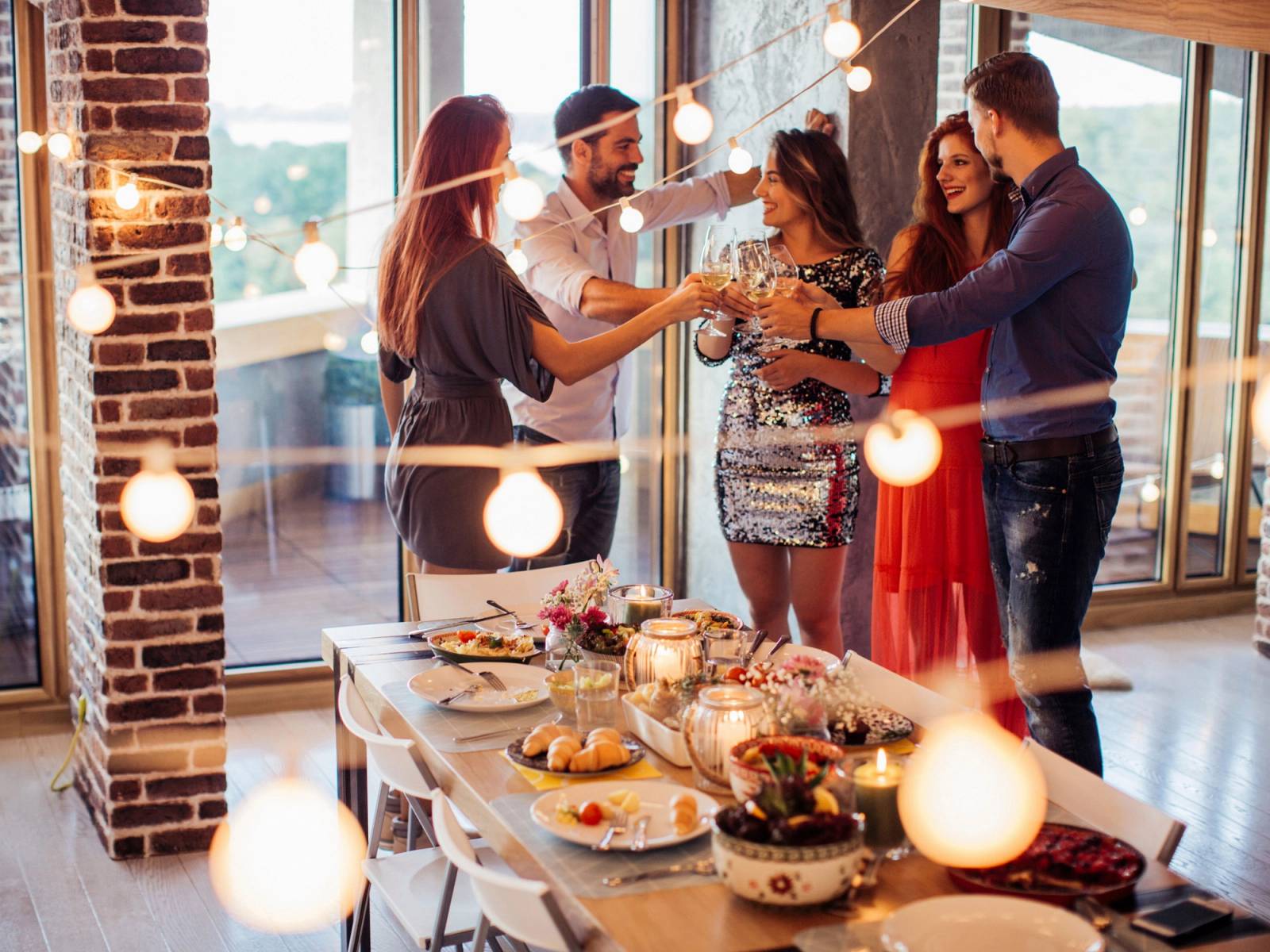 En gruppe mennesker feirer nyttårsaften med dans og fest i et rom med store vinduer og pyntede bord.