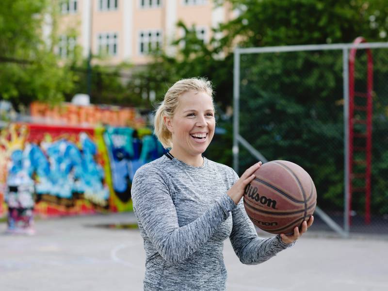 En person holder en basketball på en utendørs basketballbane med graffiti og mål i bakgrunnen.