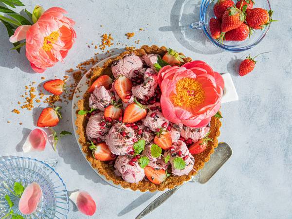 Kirsebærpai med friske jordbær og mynte på en lys bakgrunn, omgitt av blomster og jordbær i en skål.