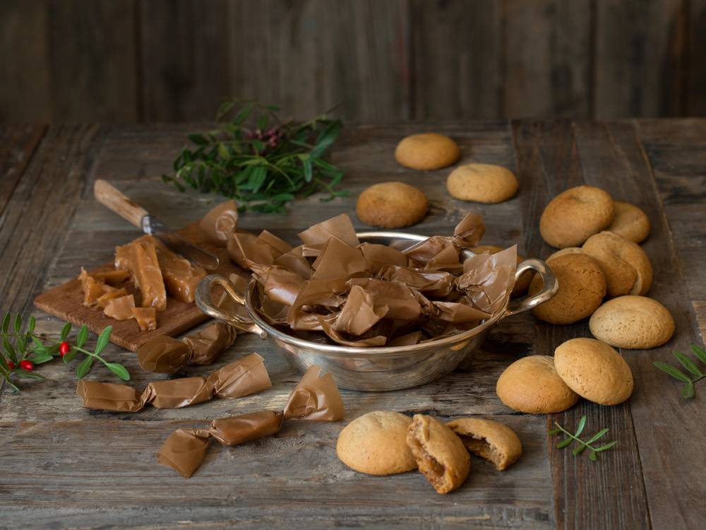 Fylte pepperkakedeiger og fløtekarameller på et trebord med grønne urter i bakgrunnen