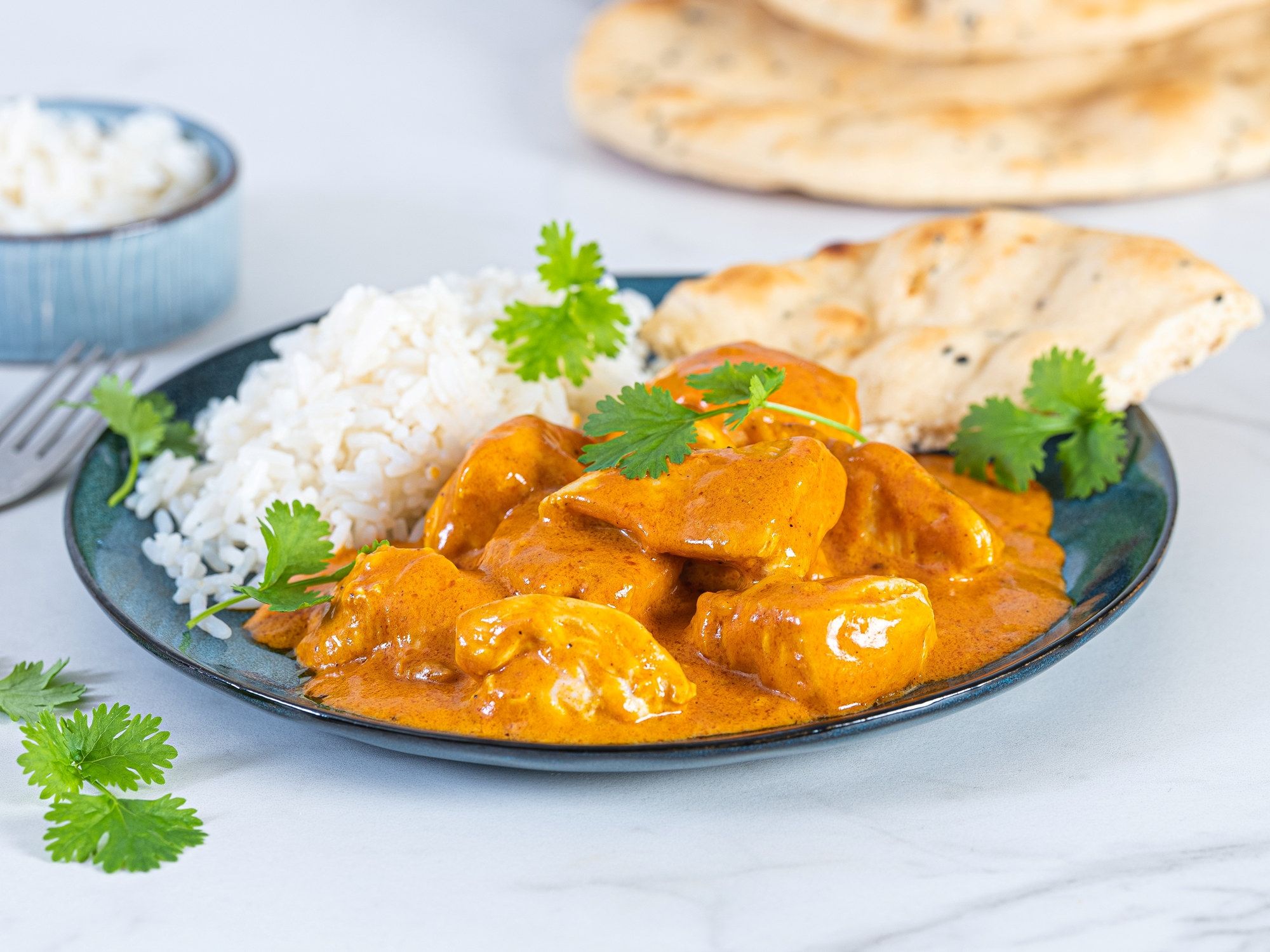 Kylling i en kremet, gul saus med ris og naanbrød på en tallerken, pyntet med frisk koriander.