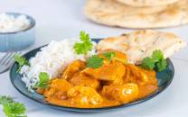 Kylling i en kremet, gul saus med ris og naanbrød på en tallerken, pyntet med frisk koriander.