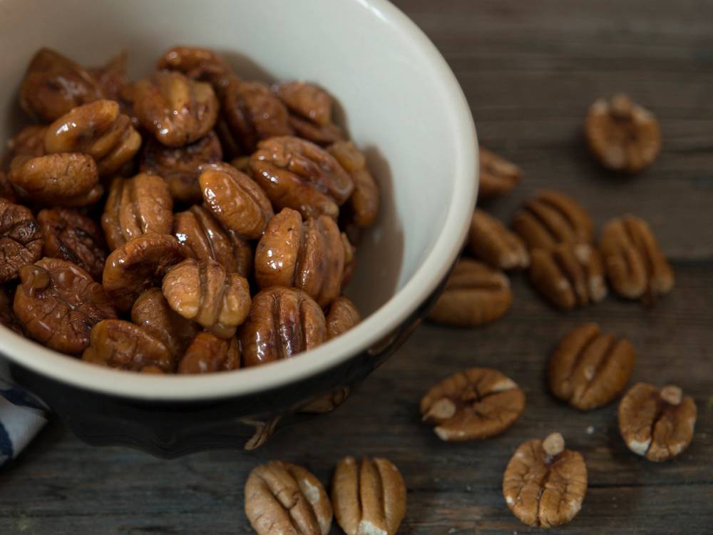 Nøtter i en hvit bolle med noen nøtter spredt rundt på en mørk treflate