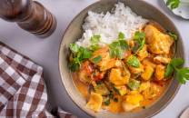 Fisk wok med rød curry servert med ris i en skål, pyntet med frisk koriander, på et bord med bestikk og en limebåt.