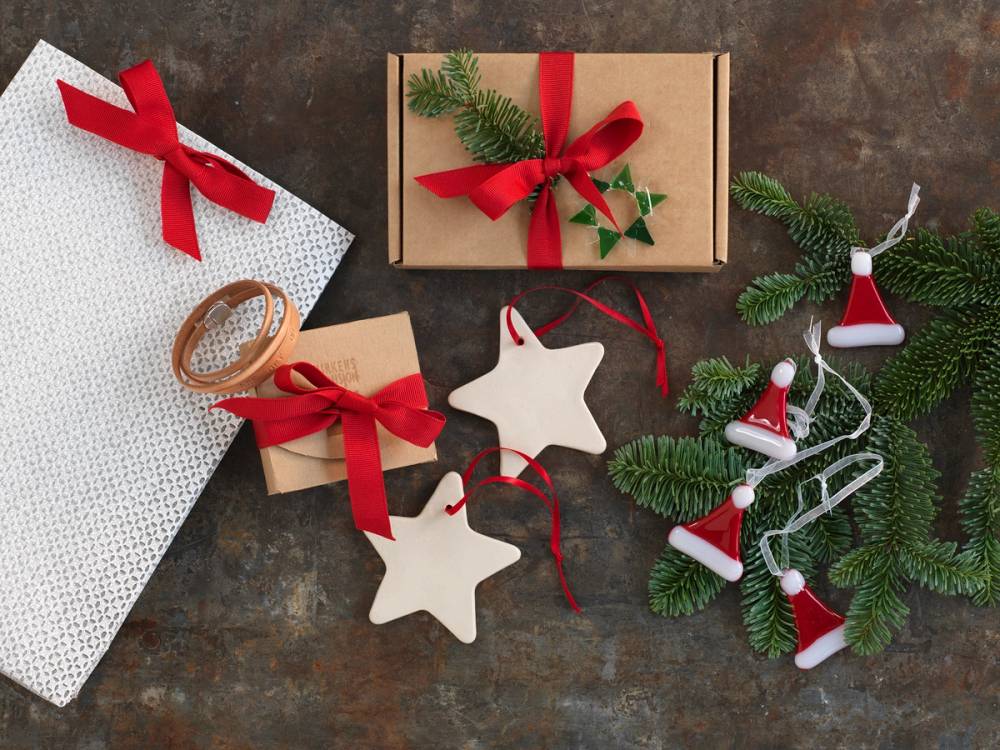 Julegaver med røde bånd, julepynt og en julegren med små bjeller på et bord.