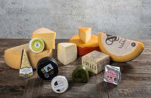 Ulike typer ost og små ostekartonger på et bord foran en grå vegg