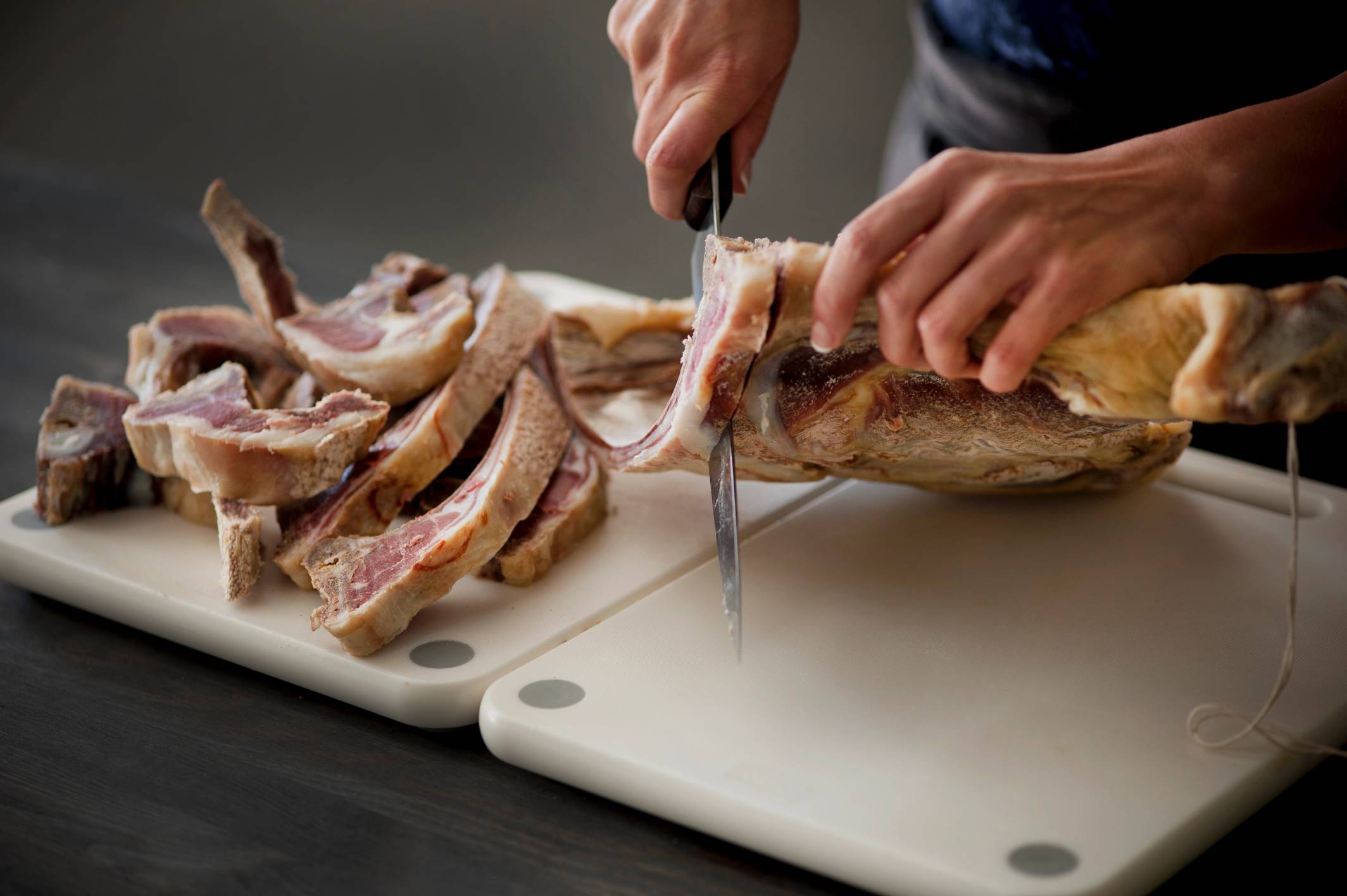 Person skjærer opp en stor fisk på et kjøkkenbord med en hvit skjærebrett.