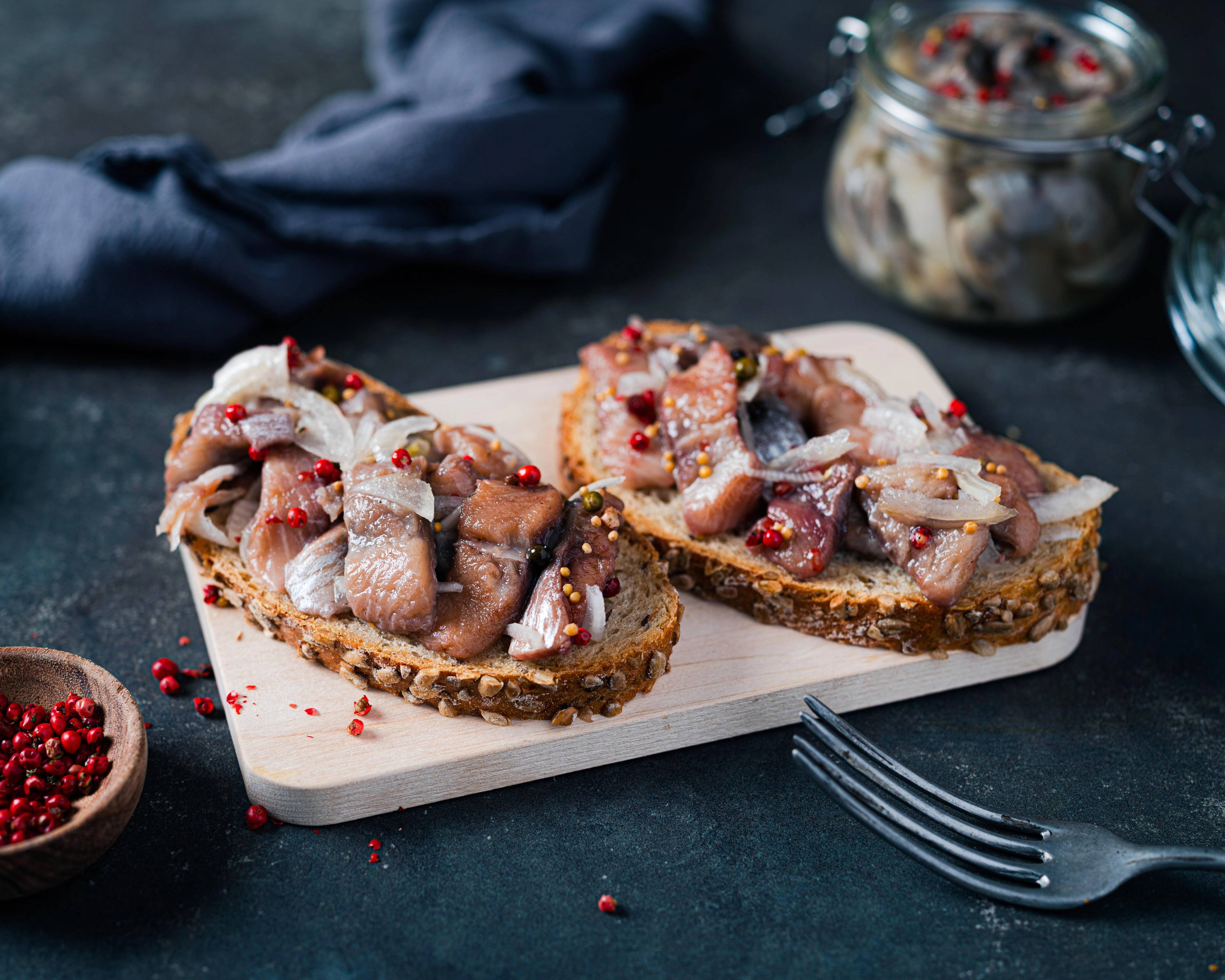 To skiver kryddersild på et skjærebrett med pepperkorn og en skål med krydder ved siden av.