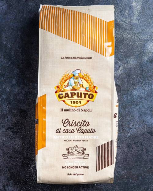 En pose med pizzamel fra Caputo, med logo og tekst på emballasjen, plassert på en mørk overflate.