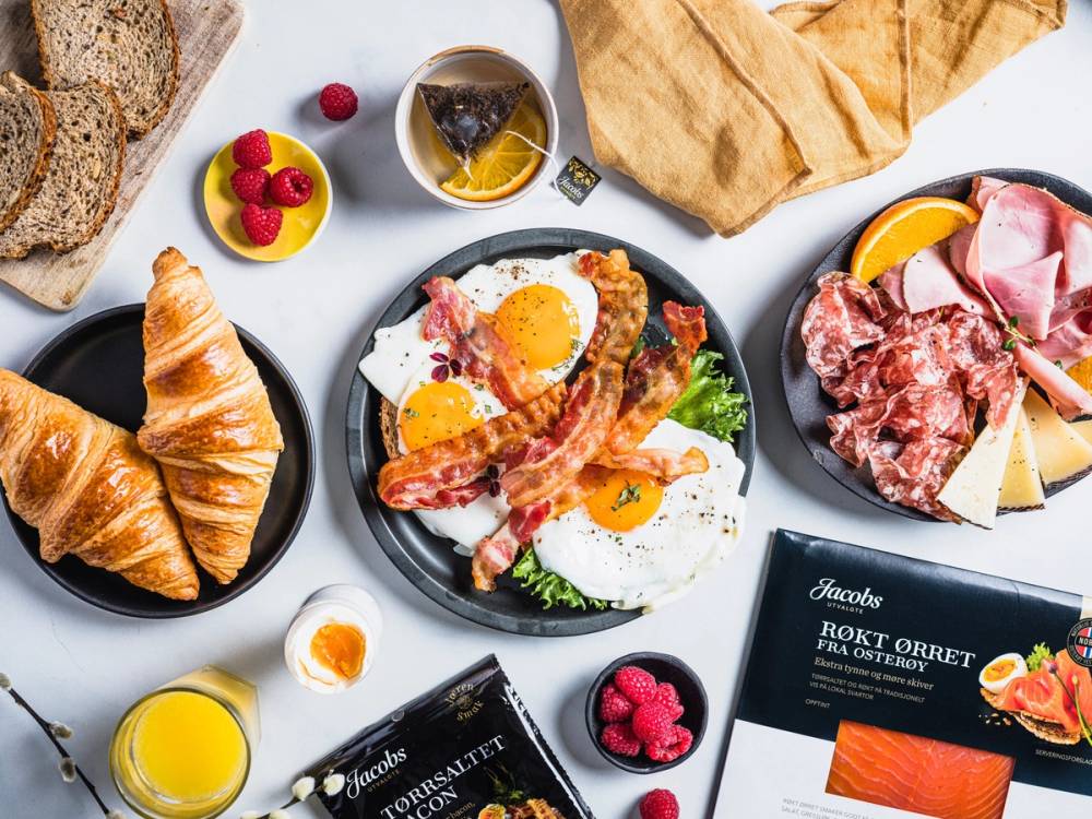 Frokostbord med egg, bacon, croissant, påskegodt og påskepynt, inkludert små bær og juice.