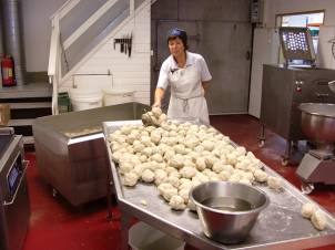 En person i hvit arbeidsuniform lager eller former deigballer på et kjøkkenbord med mange deigballer foran seg.