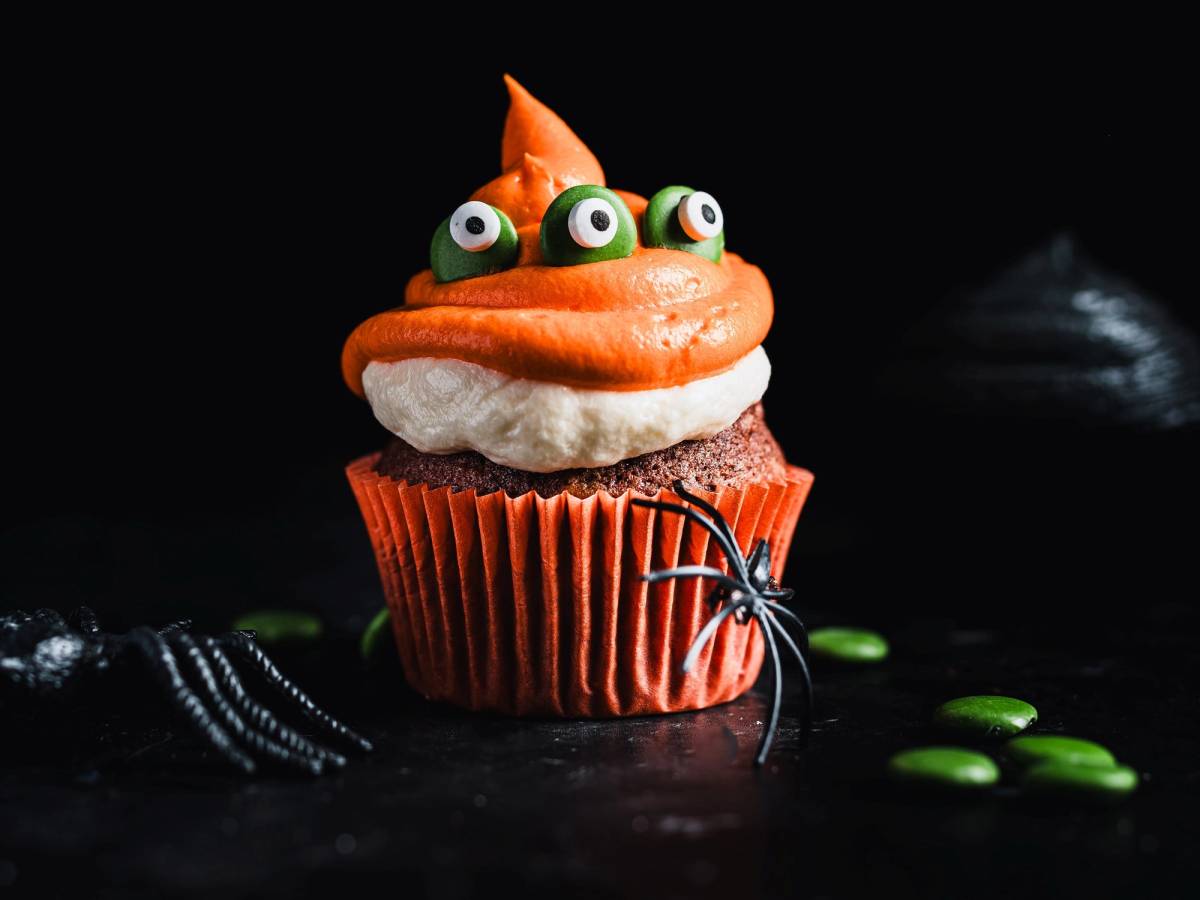 En cupcake dekorert med tre små grønne øyne og et lite oransje spisst horn, med Halloween-tema.