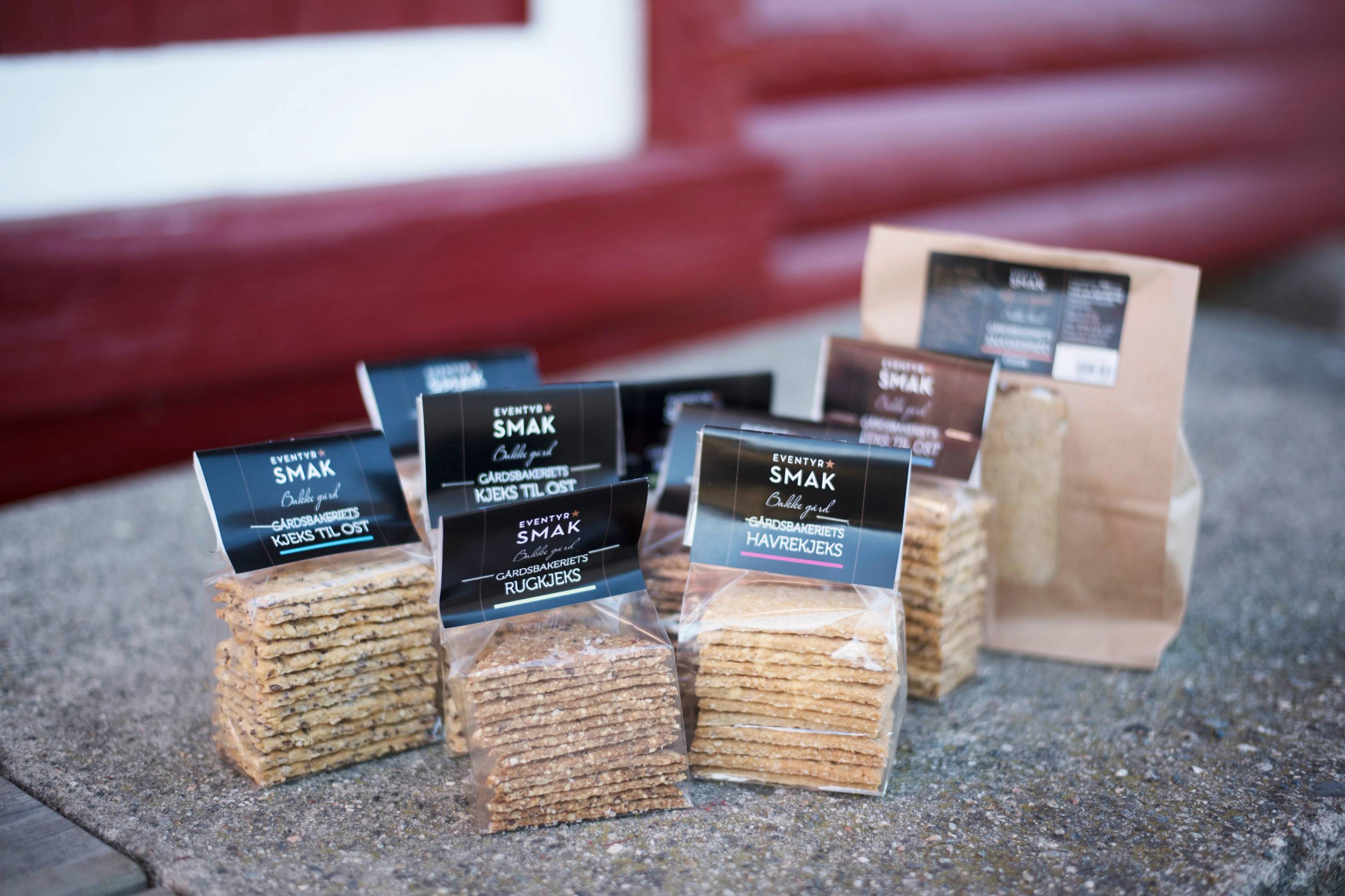 Pakker med kjeks fra Eventyrsmak, plassert på en bordflate med en pose i bakgrunnen.