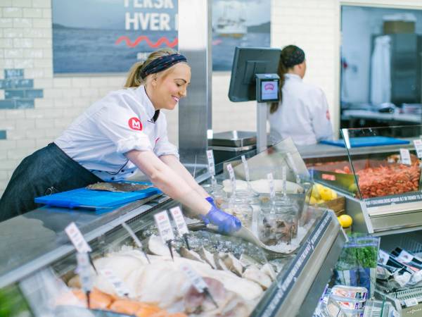 En person i butikk som selger fisk, står bak en fiskedisk med ulike typer sjømat.