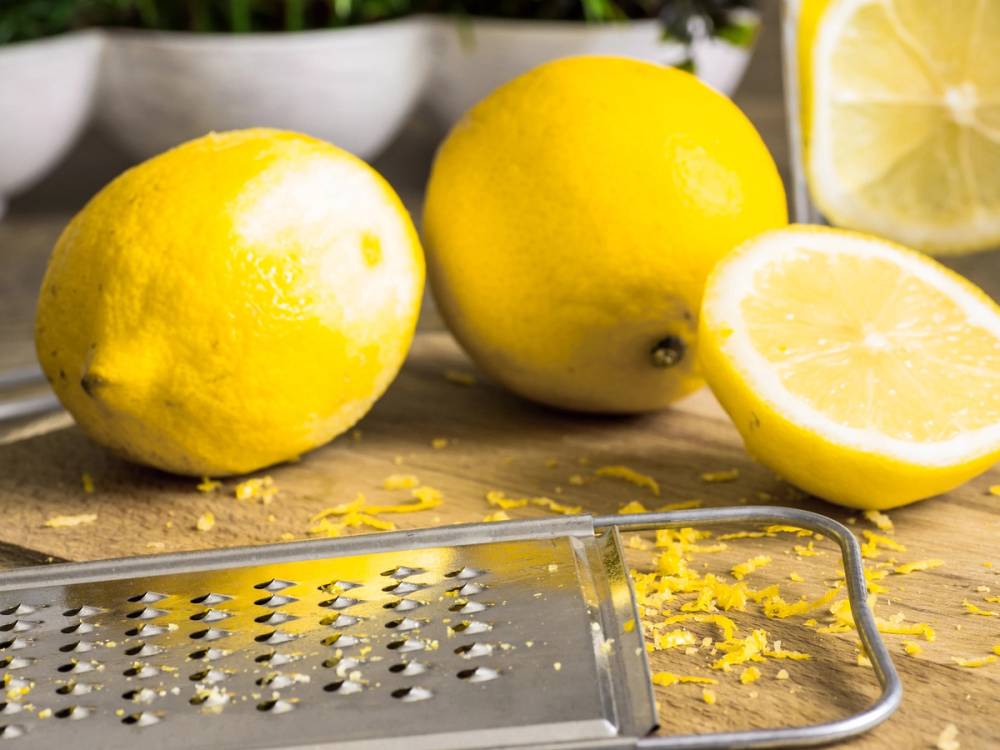 To hele sitroner og en halvert sitron på et kjøkkenbord, med et rivjern foran.