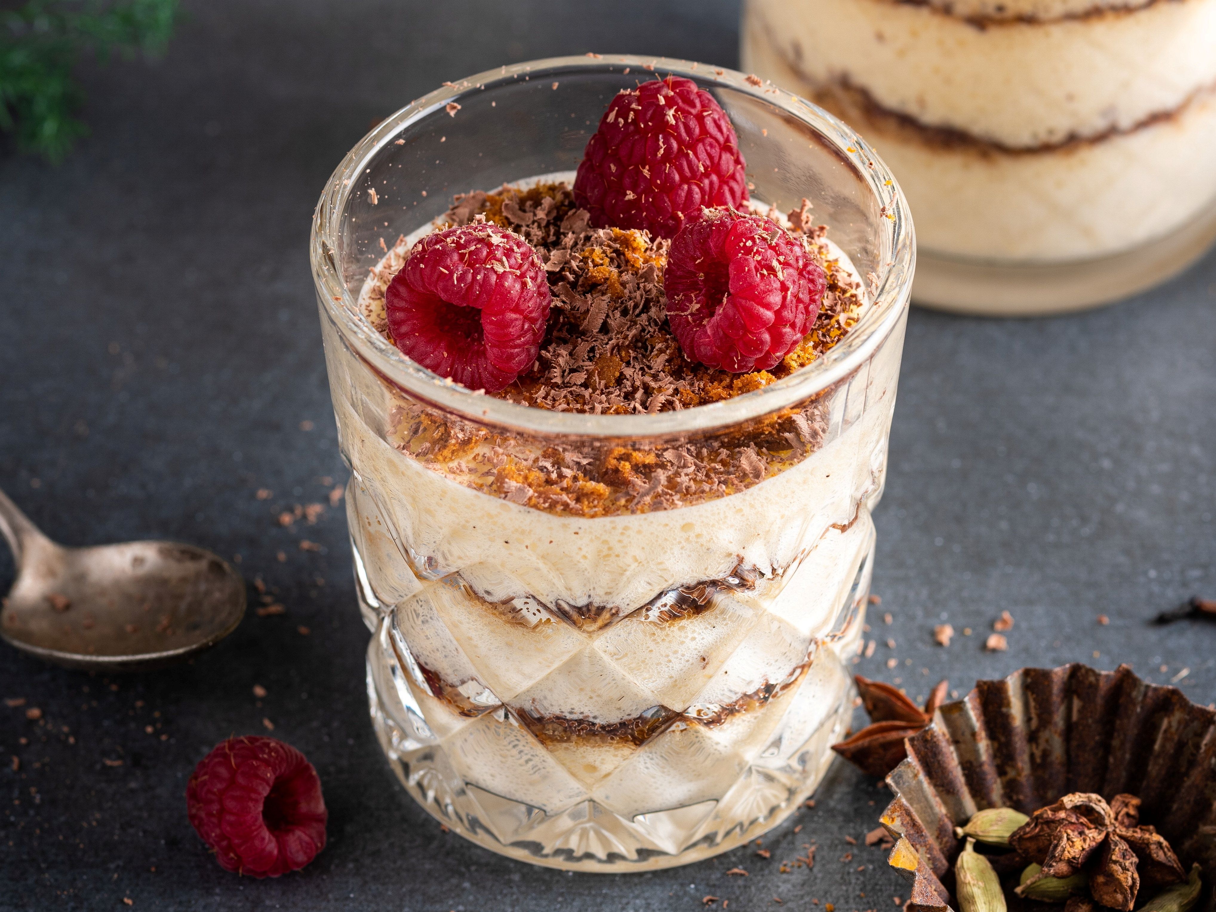 Et lagdelt dessert i et glass med krem, sjokoladekrønsj og friske bringebær på toppen.