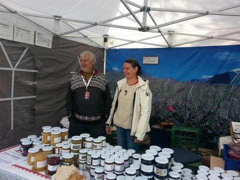 To personer står bak en bord med ulike syltetøyglass under Ottamartnan 2014, med en blå og grå teltvegg i bakgrunnen.