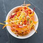 En bol med råkostsalat med strimler av gulrot, rødbete og kål, pyntet med urter.