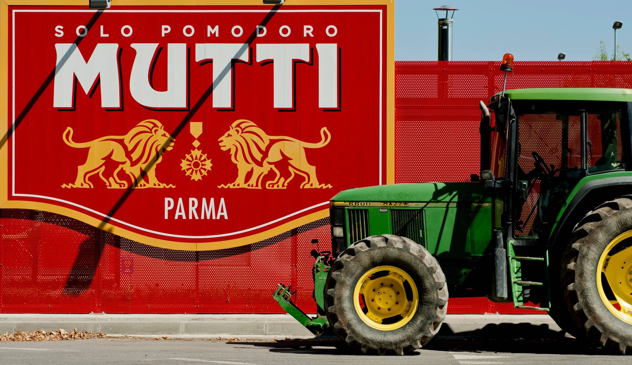 En grønn og gul traktor står foran en stor rød vegg med logoen til Mutti og Parma, Italia.