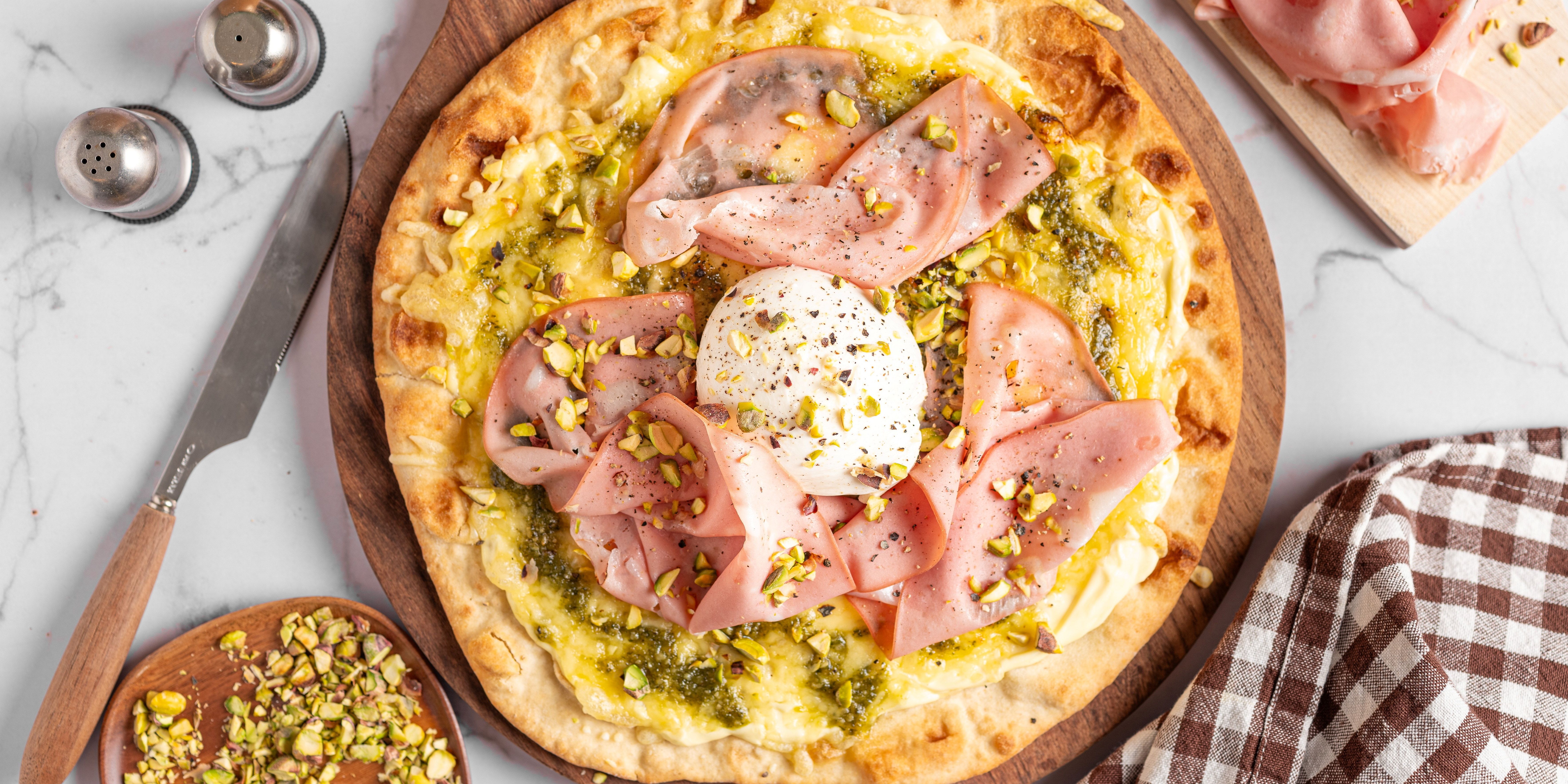 Pizza med mortadella, skinke og et speilegg på toppen, ser varm og innbydende ut.