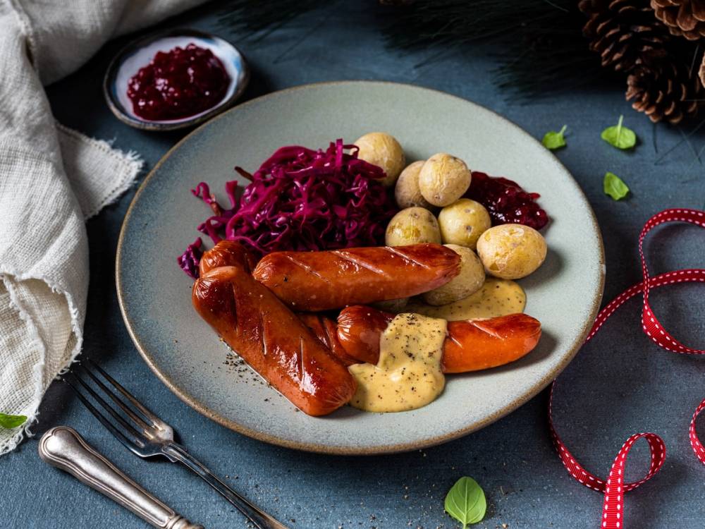 Søndagstallerken med pølser, kokte poteter, rødkål og sennepssaus på et fat, omgitt av juledekorasjoner.