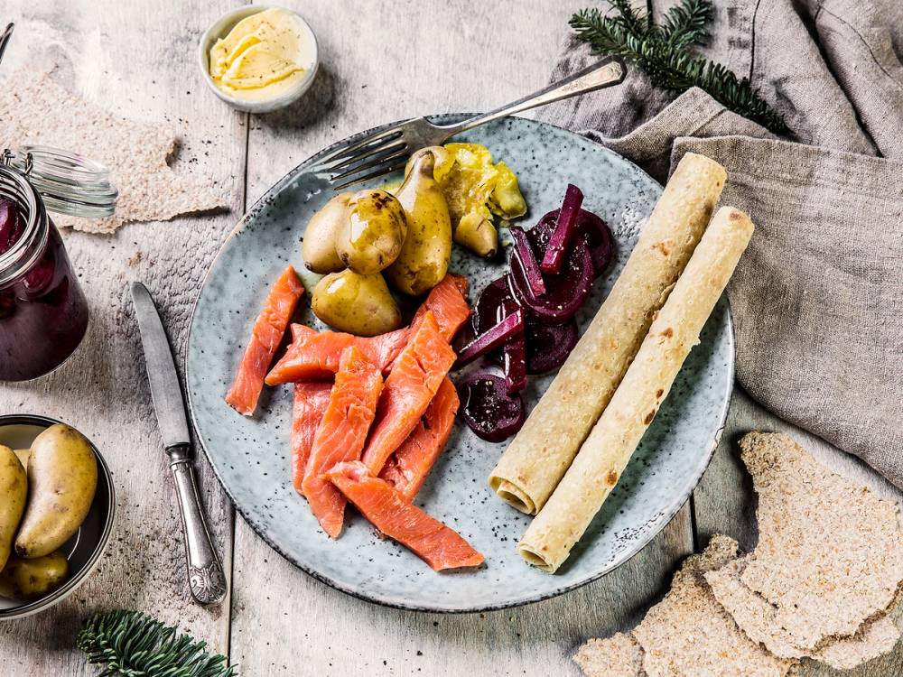 Rakfisk servert med grønnsaker og flatbrød på en tallerken, omgitt av tradisjonelle norske tilbehør.