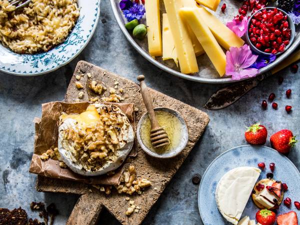 Et ostefat med ulike oster, frukt og honning, samt et dessertfat med ost og nøtter på et bord.