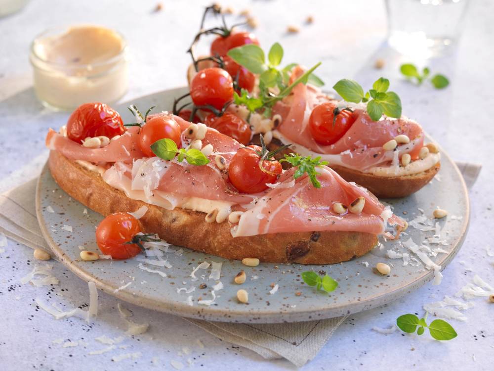 Bruschetta med spekeskinke, mozzarella og cherrytomater på en tallerken med urter og olivenolje.