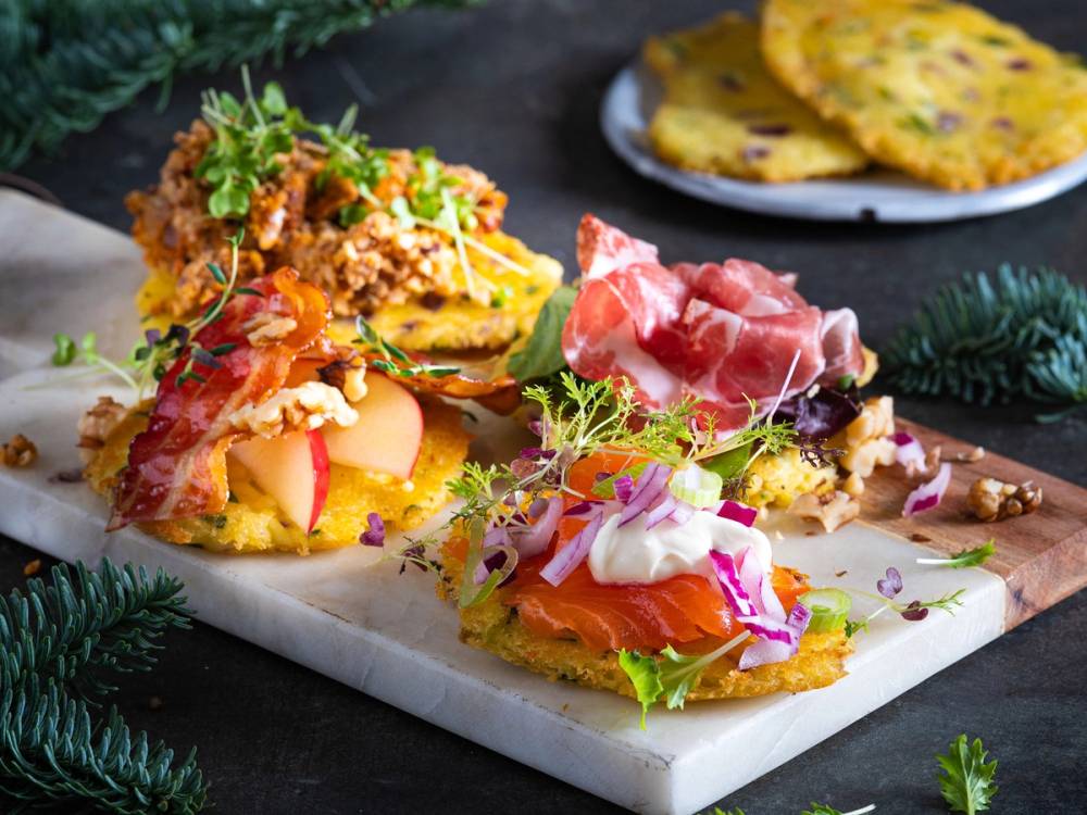 Rester av julemat med ulike pålegg og tilbehør på et serveringsfat, med noen pannekaker i bakgrunnen