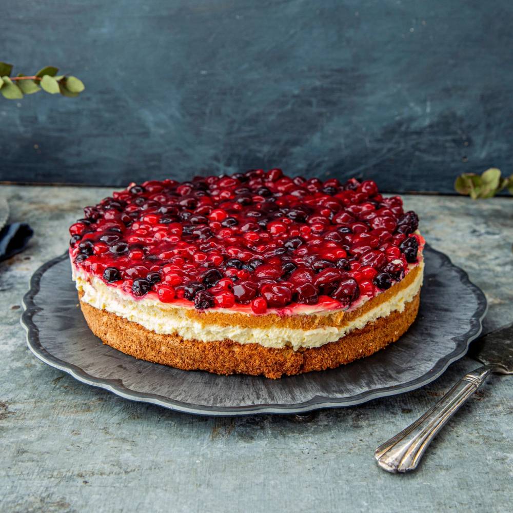 En rund vaniljekake med bær på toppen, servert på en svart tallerken med en sølvskje ved siden av.