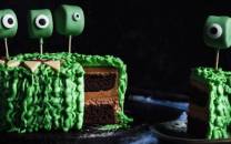 En kake dekorert med grønne og svarte halloween-monstre, der en del av kaken er skåret ut for å vise sjokoladekrem og kakebunn inni.