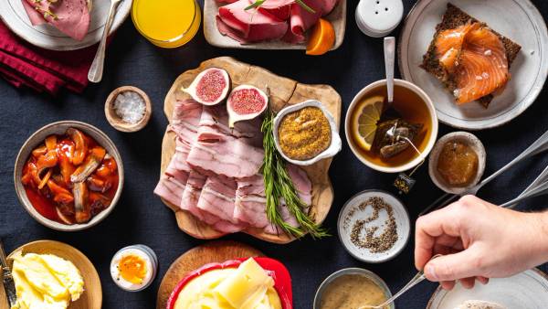 Et julefrokostbord med ulike retter som spekemat, gravlaks, og tilbehør, med en person som serverer mat.