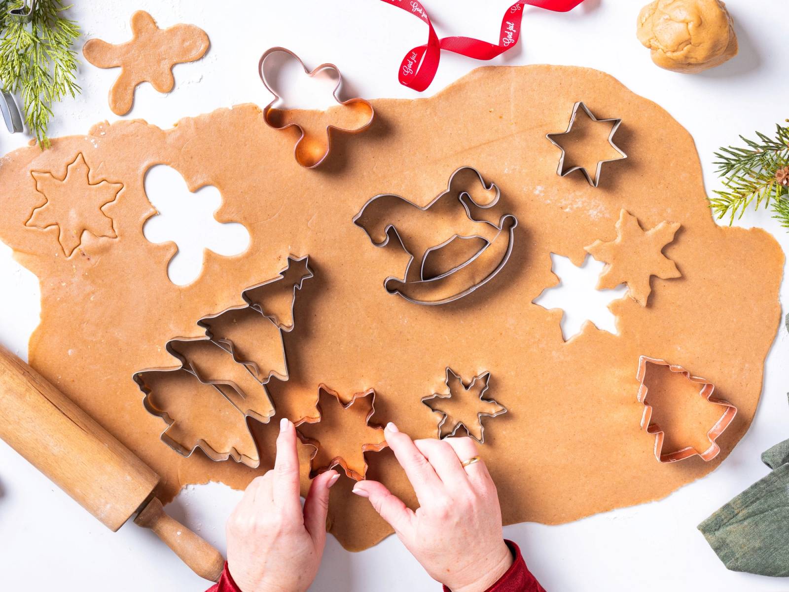 Barn som lager pepperkaker med ulike former på et kjøkkenbord dekket med pepperkakedeig og utstikkere.
