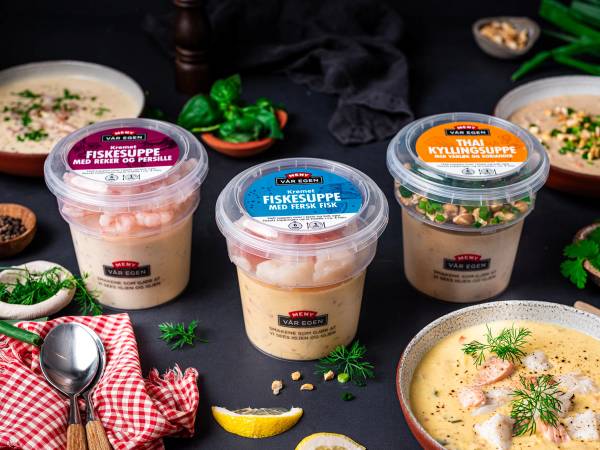 To kopper med fiskesuppe og en skål med kyllingsuppe omgitt av grønnsaker og sitronbiter på et bord.